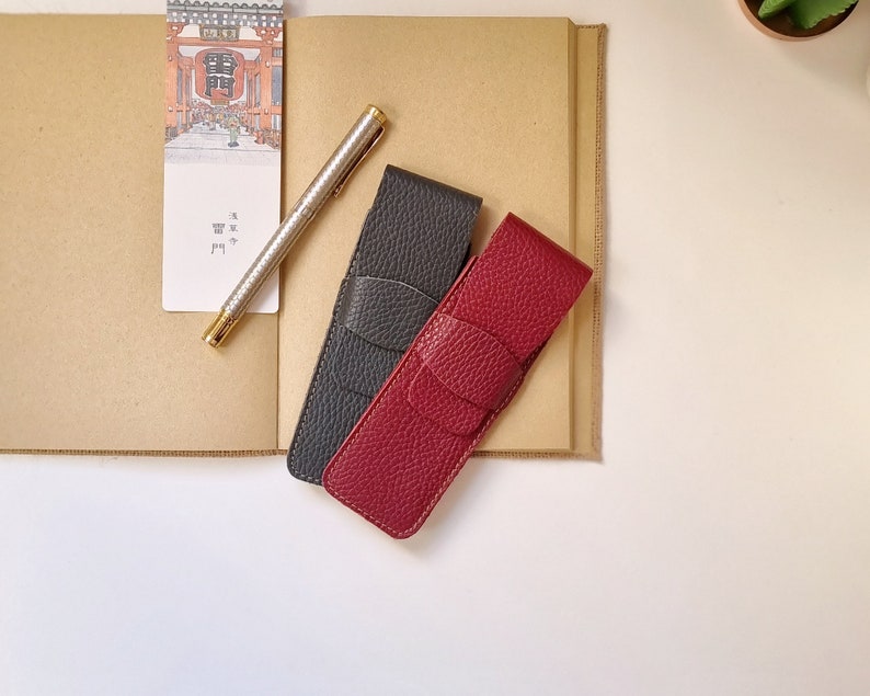 two leather pen holders, one in burgundy and the other in gray. each holds two pens. They close with a flap. The leather with which they are handmade is of high quality and very soft.