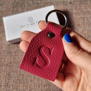 以下が含まれることがあります： 銀色のキーリングと、前面に「S」の文字が刻印された赤い革のキーホルダーです。