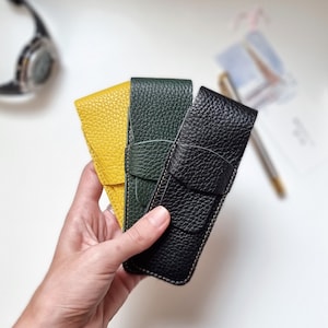 monogram pen sleeve pouch in three different colors made of leather. leather pouch in yellow color, leather pouch in dark green and the last pen case in black