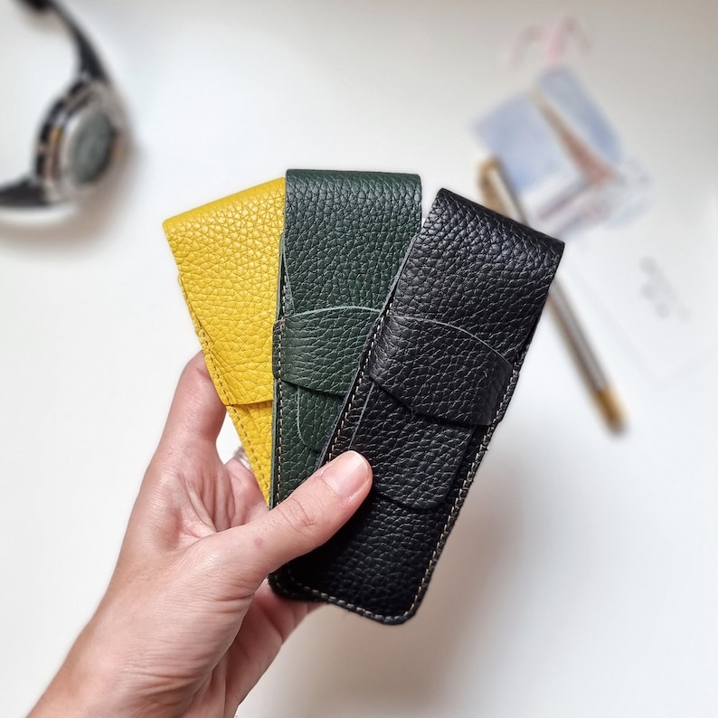 monogram pen sleeve pouch in three different colors made of leather. leather case in yellow color, leather pouch in dark green and the last pen case in black