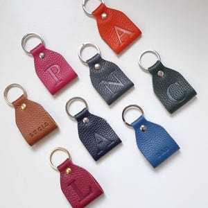 eight colorful key rings on white background, all key rings are full grain leather, engraved with initial or short name. Personalized keychain colors are brown, pink, orange, dark green, blue, gray, burgundy and navy blue.