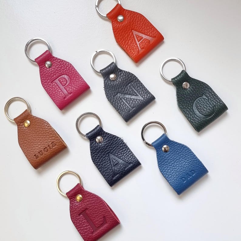 eight colorful key rings on white background, all key rings are full grain leather, engraved with initial or short name. Personalized keychain colors are brown, pink, orange, dark green, blue, gray, burgundy and navy blue.