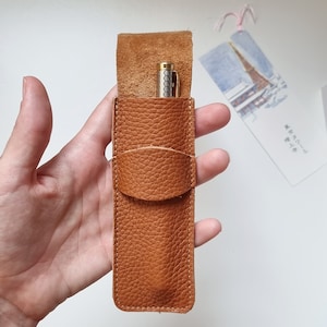 Leather pen case in havana or brown color. The pen pouch is shown open, with a pen inside, you can see that it can hold two pens. This leather pen pouch closes with a flap.