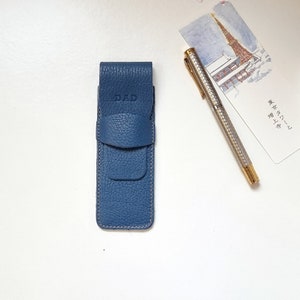 blue leather pencil case on a table and a stylus pen next to it. On the pen case is engraved the word DAD.