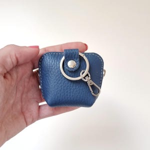 Hand holding navy leather AirPods pouch with keyring, compact and portable