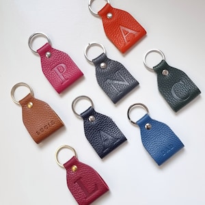 eight colorful key rings on white background, all key rings are full grain leather, engraved with initial or short name. Personalized keychain colors are brown, pink, orange, dark green, blue, gray, burgundy and navy blue.