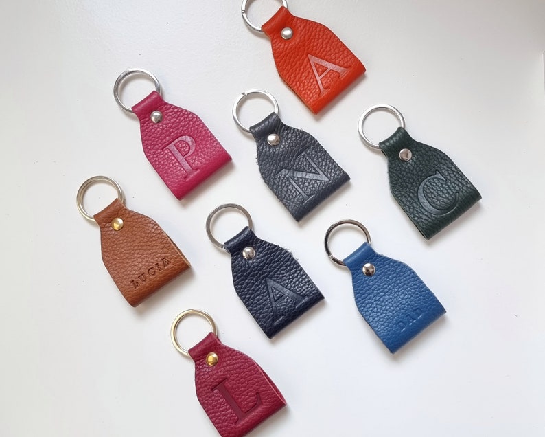 eight colorful key rings on white background, all key rings are full grain leather, engraved with initial or short name. Personalized keychain colors are brown, pink, orange, dark green, blue, gray, burgundy and navy blue.