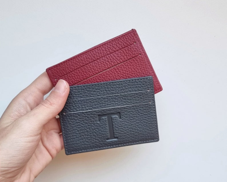 This card holder has two card slots. In a hand are shown two plain color cardholders, one in gray and the other in burgundy. The leather used for these cardholders is high quality full grain leather.