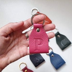 on one hand is a small fuchsia pink full-grain soft leather key ring engraved with the uppercase letter P.