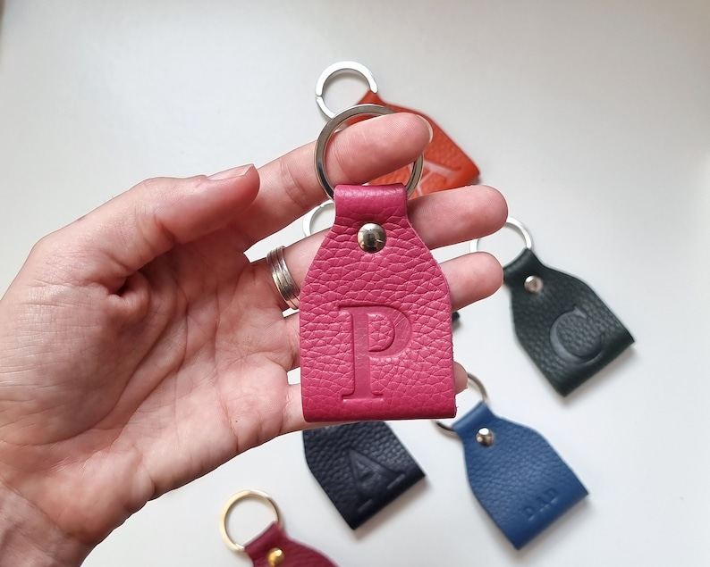 on one hand is a small fuchsia pink full-grain soft leather key ring engraved with the uppercase letter P.