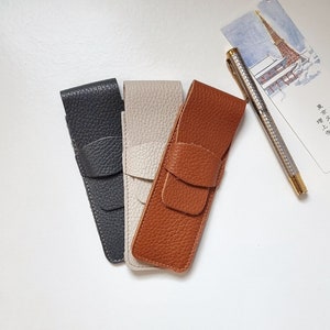 three leather pen pouch in thre different colors, one in gray color, one leather pen case in light beige color and one pen case in havana or brown color.