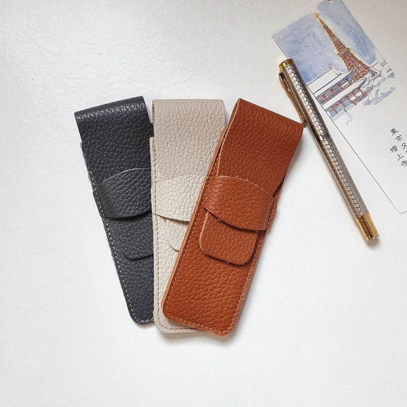 handcrafted leather pen pouch. There are three pen cases, one in gray color, one leather pen case in light beige color and one pen case in havana or brown color.
