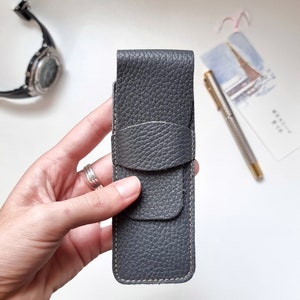 one hand shows a very soft, full grain leather pen case in gray color for those who love writing.