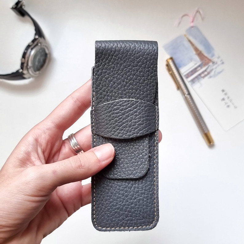 one hand shows a very soft, full grain leather pen case in gray color for those who love writing.