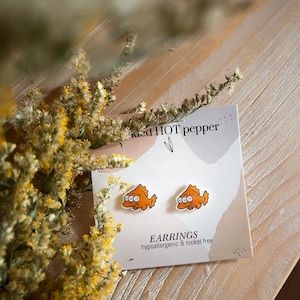 May include: Orange fish-shaped stud earrings on a white card with the text "Red HOT pepper" and "EARRINGS hypoallergenic & nickel free".