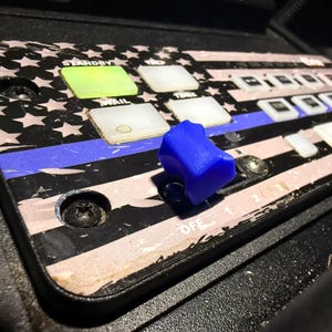 Könnte beinhalten: Nahaufnahme eines schwarzen Bedienfelds mit einem blau-weißen amerikanischen Flaggenmuster. Das Panel hat mehrere Knöpfe und einen blauen Kippschalter mit der Aufschrift "OFF".