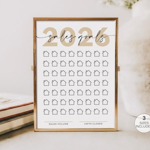 May include: A framed print with a gold-colored frame. The print features the text "Sales Goals 2026" in a gold color, along with rows of small house icons. The bottom of the print has the text "Sales Volume" and "Units Closed".
