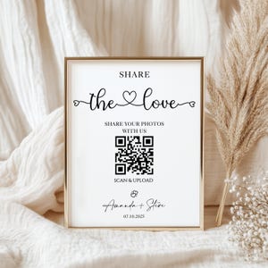 May include: A framed sign with gold trim and white background. The sign reads "SHARE the love" with a heart symbol. Below is a QR code and the text "SHARE YOUR PHOTOS WITH US" and "SCAN & UPLOAD". The names "Amanda + Steve" and the date "07.10.2025" are at the bottom.