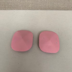 May include: Two pink square-shaped tile-like objects with a raised pyramid shape in the center.