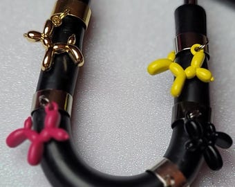 May include: A black stethoscope with multiple charms attached. The charms are shaped like balloon animals, including a yellow dog, a pink dog, and a gold dog.