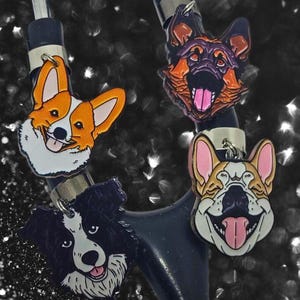 Puede incluir: Cuatro colgantes con temática de perros con fijaciones plateadas. Los colgantes presentan un Corgi, un Pastor Alemán y un Border Collie, cada uno con una expresión sonriente. Los colgantes Corgi son naranjas y blancos, mientras que el Pastor Alemán es negro, naranja y morado.