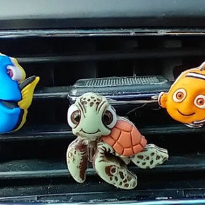 Puede incluir: Tres adornos de ambientador de coche con personajes de la película Buscando a Nemo. Los adornos son un Dory azul y amarillo, un pez payaso naranja y blanco y una tortuga marina verde y marrón.