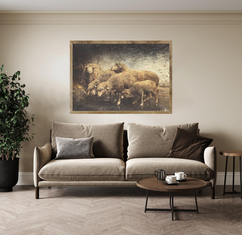May include: A framed sepia-toned print of a group of sheep standing in a field. The sheep are brown and white and have fluffy wool. The print is set against a beige wall above a brown couch.