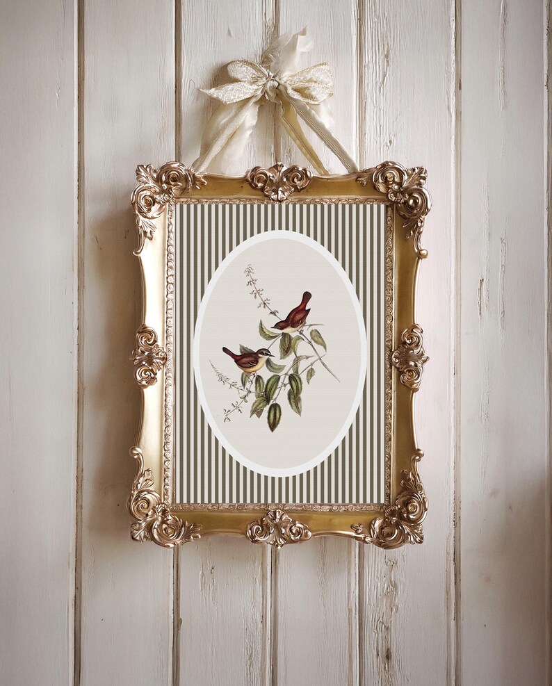 May include: Ornate gold framed artwork featuring an oval print of two birds perched on a leafy branch. The background has vertical stripes in olive green and cream. The frame is suspended by a cream-colored ribbon.