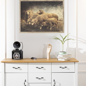 May include: A framed vintage-style print of a group of sheep in a field. The print has a distressed, textured look and is displayed on a white wall above a dresser.