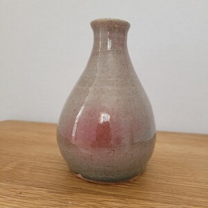 Könnte beinhalten: Eine handgefertigte Keramikvase mit bauchigem Körper und schmalem Hals. Die Vase hat eine gesprenkelte, gedämpfte Farbpalette mit Grautönen, Rosa und Grün. Die Vase ist etwa 15 cm hoch.