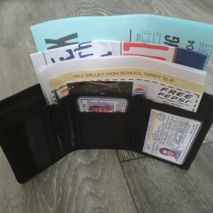 May include: A black trifold wallet with a driver's license, a credit card, and a school tardy slip inside. The tardy slip is from Hill Valley High School.