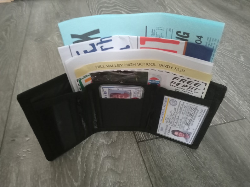 May include: A black trifold wallet with a driver's license, a credit card, and a school tardy slip inside. The tardy slip is from Hill Valley High School.