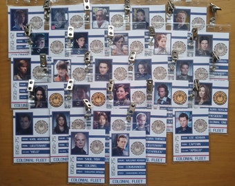 May include: A collection of 16 white and blue plastic ID badges with photos of different people. Each badge has a name, rank, and post printed on it. The badges are hanging from silver clips.