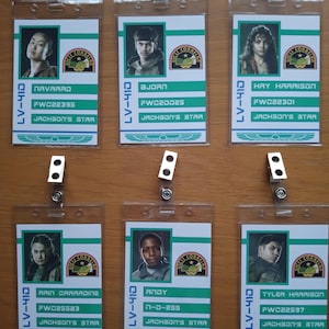 Puede incluir: Seis insignias de identificación de plástico de colores con fotos de personas y texto. El texto incluye nombres, títulos y códigos. Las insignias están sobre una superficie de madera.