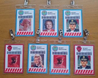 May include: Six plastic security identification badges with red and white stripes, blue borders, and a cartoon elephant logo. Each badge has a different person's photo and name, including "Satia Zevo", "Leland Zevo", "Patrick Zevo", and "Gwen Tyler".