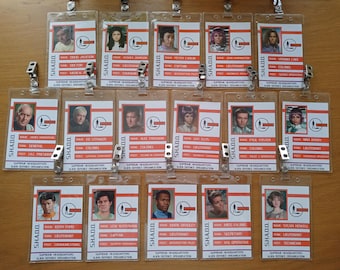 May include: A set of 15 plastic ID badges with red and white text. Each badge features a photo of a person and their name, rank, and department. The text on the badges reads "SHADO" and "Supreme Headquarters Alien Defence Organisation".