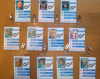 May include: A set of 10 colorful ID badges featuring characters from the TV show Thunderbirds. Each badge has a character's name, role, and the words "F.A.B." and "International Rescue".