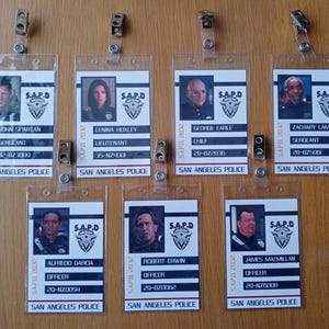 Op de afbeelding: Zeven rechthoekige identificatiebadges van de San Angeles Police met doorzichtige plastic houders en metalen clips. Elke badge bevat een portret, het S.A.P.D-logo, de naam, de rang en het identificatienummer van de betreffende persoon.