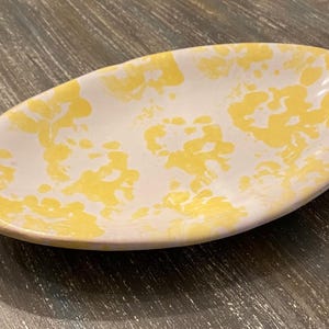 May include: Oval-shaped ceramic dish with a white base and a yellow floral pattern. The dish has a slightly raised edge and is suitable for serving appetizers or small dishes. The design is reminiscent of a sunny day.