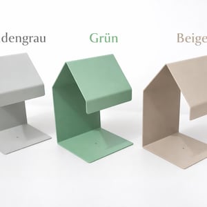 May include: Three metal bookends in different colors: Seidengrau (light gray), Gr&uuml;n (green), and Beige (tan). Each bookend has a unique angular design with a flat base and a raised top section, ideal for organizing books.