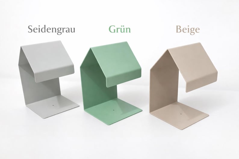 May include: Three metal bookends in different colors: Seidengrau (light gray), Gr&uuml;n (green), and Beige (tan). Each bookend has a unique angular design with a flat base and a raised top section, ideal for organizing books.