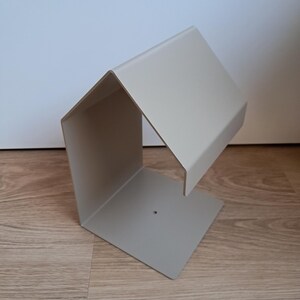 May include: A modern, light gray metal desk organizer with a geometric design. The organizer has a rectangular base and a slanted top, creating a unique, open-sided storage space. The minimalist design is suitable for office or home use.