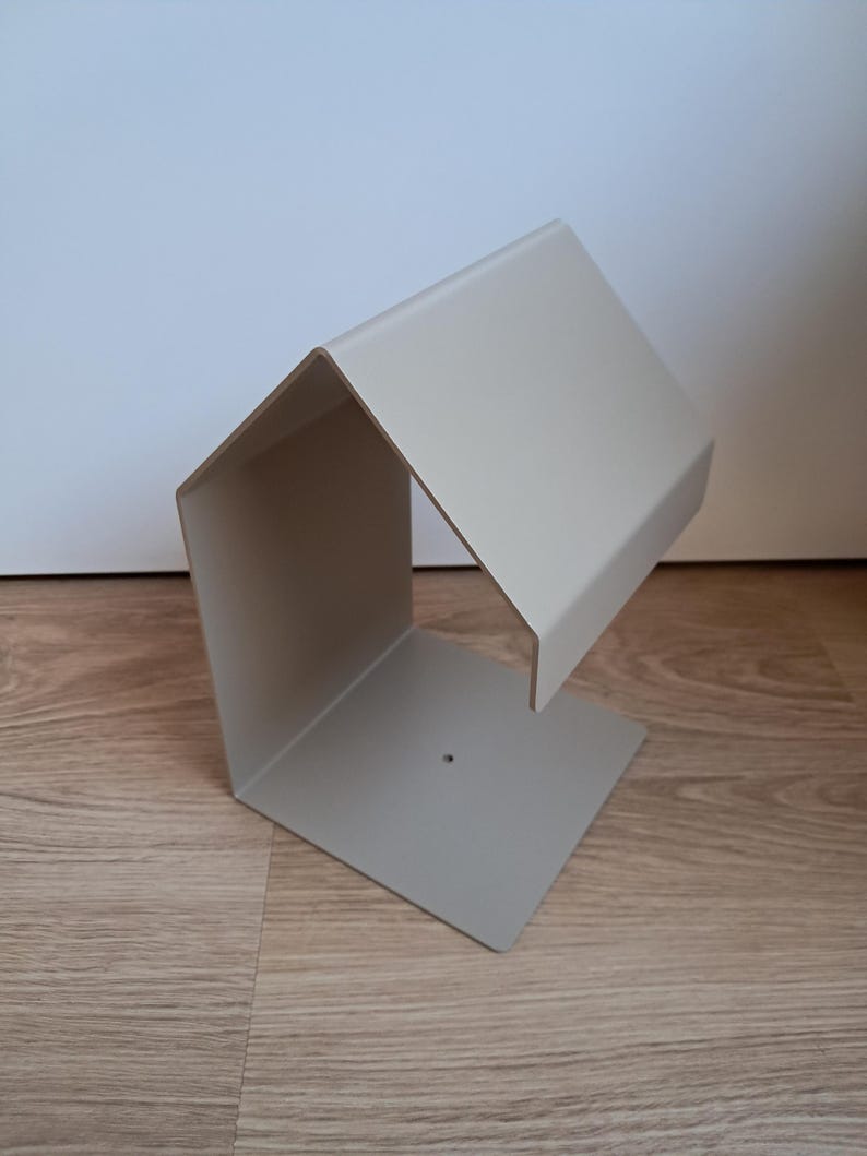 May include: A modern, light gray metal desk organizer with a geometric design. The organizer has a rectangular base and a slanted top, creating a unique, open-sided storage space. The minimalist design is suitable for office or home use.