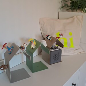 May include: Three metal house-shaped bookends in gray and green, each with a small figurine on the roof. A canvas pillow with the word "ki" in neon yellow is in the background.