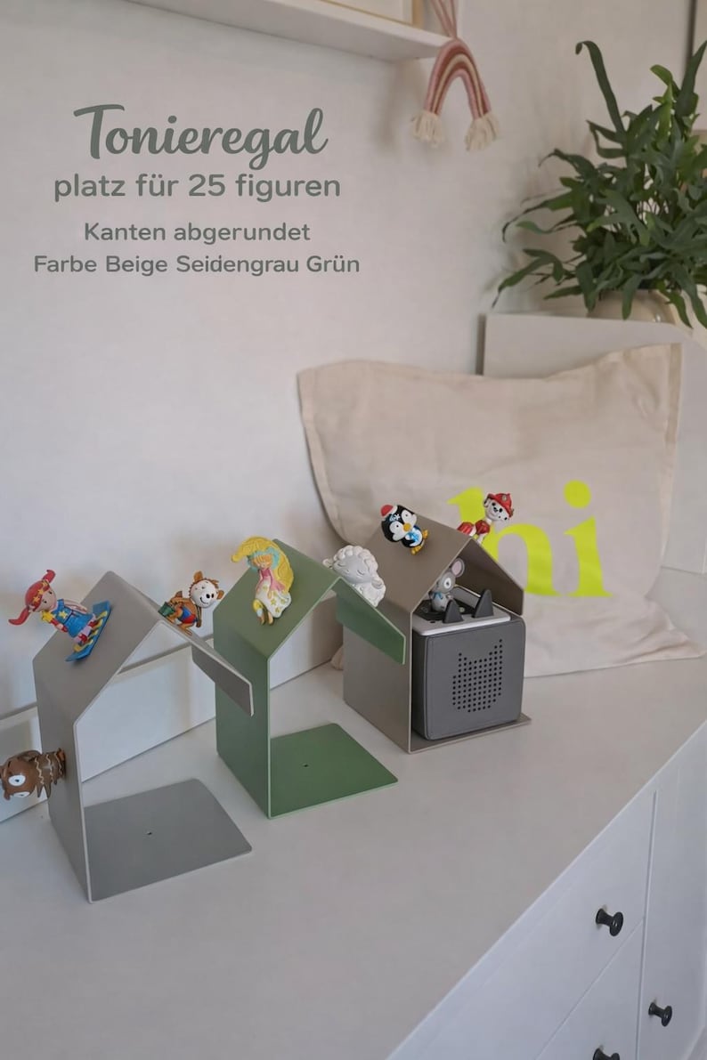 May include: A display shelf in the shape of a house, holding small figurines. The shelf is in shades of gray and green. The text on the wall says "Toniergal platz f&uuml;r 25 figuren".