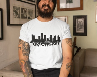 May include: A white t-shirt with a black graphic of a city skyline and the text "Screwston". The person wearing the shirt has a black beanie and tattoos on their arms.