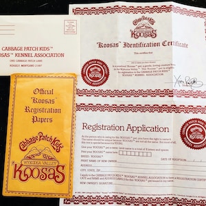 Peut inclure: Un certificat d'enregistrement jaune et rouge 'Koosas' de Cabbage Patch Kids avec le texte 'Official Koosas Registration Papers' et un logo de chaîne de montagnes rouge avec le texte 'Cabbage Patch Kids Wykosa Valley Koosas'.