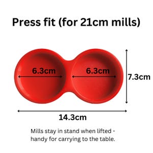 May include: A red double-cup holder for 21cm mills with a press fit design. The unit measures 14.3cm in total width and 7.3cm in height, with each cup having a 6.3cm diameter. The text reads: Press fit (for 21cm mills) and Mills stay in stand.