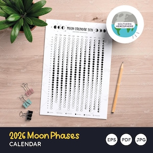 Op de afbeelding: Een witte 2026 Maanfasenkalender met een Southern Hemisphere-afbeelding. De kalender toont maanfasen in zwart en wit. Een potlood, paperclips en een potplant zijn ook zichtbaar.