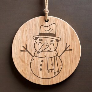 May include: A wooden round ornament with a laser-engraved design of a smiling snowman wearing a hat and scarf.